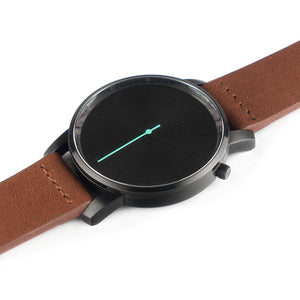 All black Hervor watch with fox brown leather strap and a turquoise accent second hand