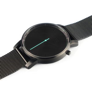 All black Hervor watch with black metallic mesh strap and a turquoise accent second hand