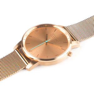 All rose gold Hervor watch with rose gold metallic mesh strap and a turquoise accent second hand